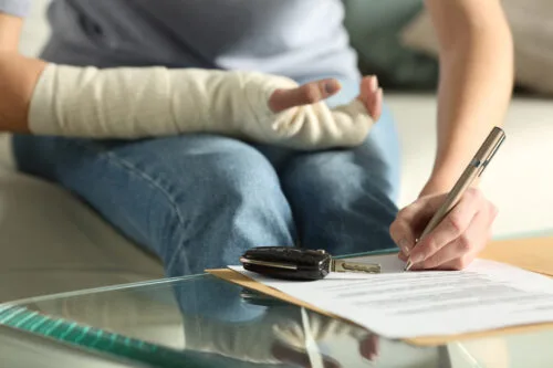 A person with their arm in a cast is using their other hand to fill out forms on a table.