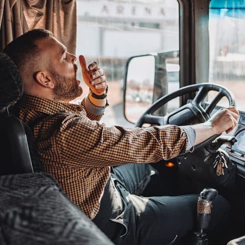 An Alabama truck driver yawns at the wheel of his vehicle, indicating drowsy driving which is one of the most common causes of semi-truck accidents.
