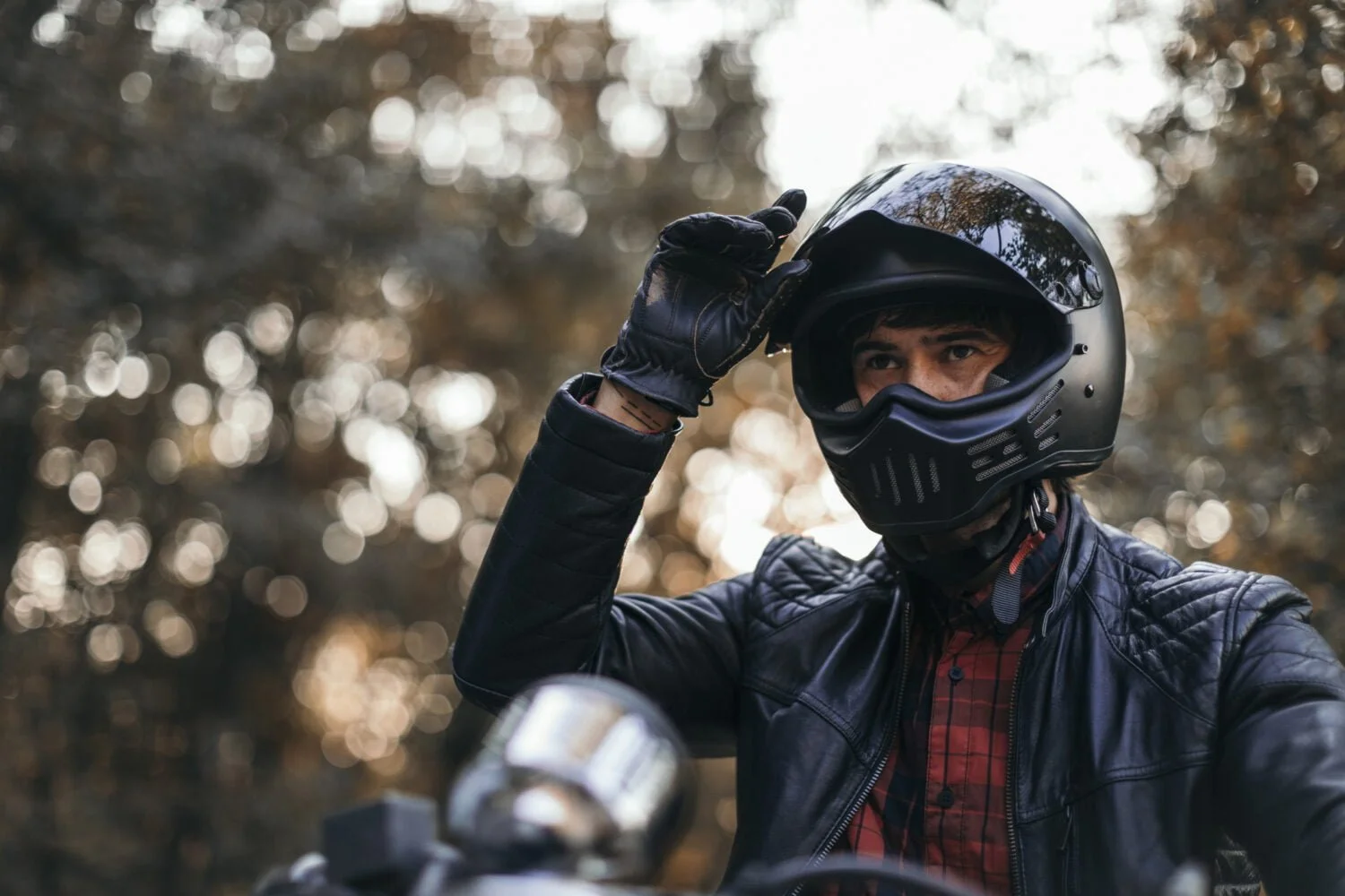 A motorcycle rider in full gear is about to pull the visor down on his helmet before going for a ride.