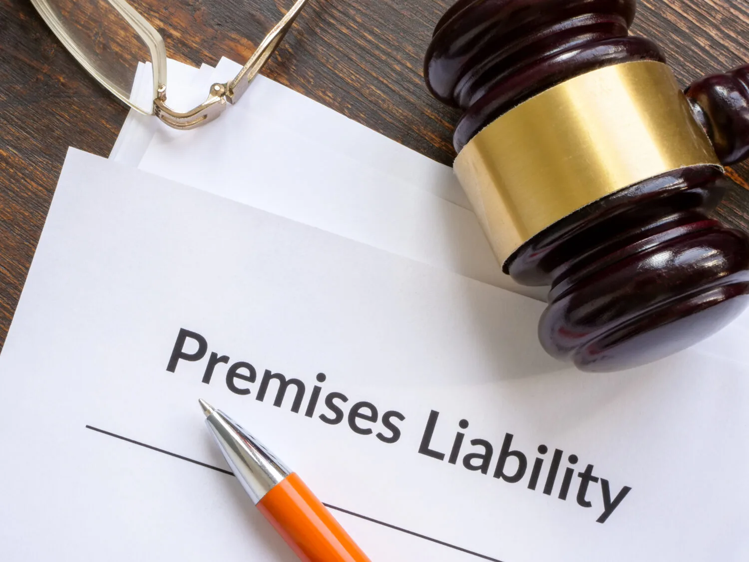A pair of glasses, a pen, and a gavel lay on a stack of documents with “Premises Liability” on the first page.