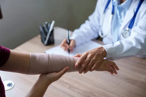 A person with a bandaged arm is examined by a doctor who is taking notes.