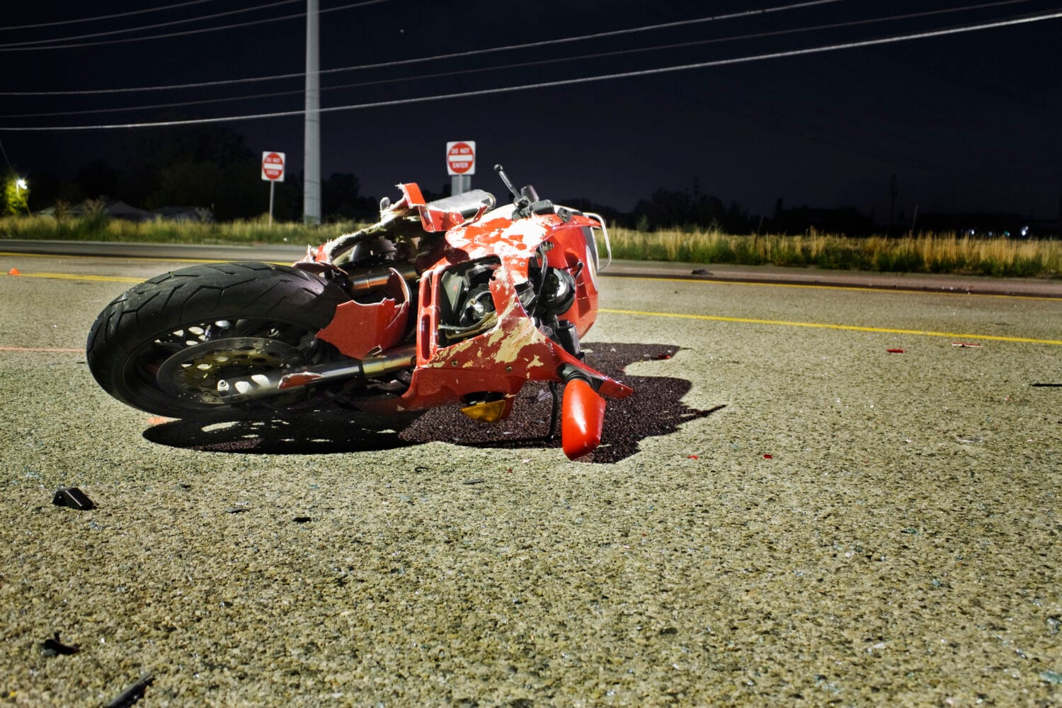 A wrecked red motorcycle on the road at night.