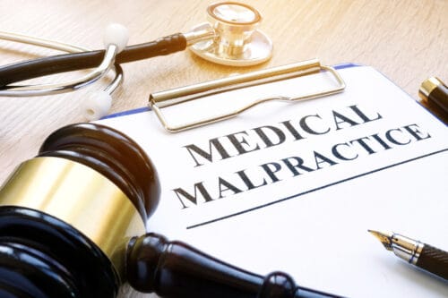 A clipboard with a paper labeled “MEDICAL MALPRACTICE”, a pen, a stethoscope, and a gavel.