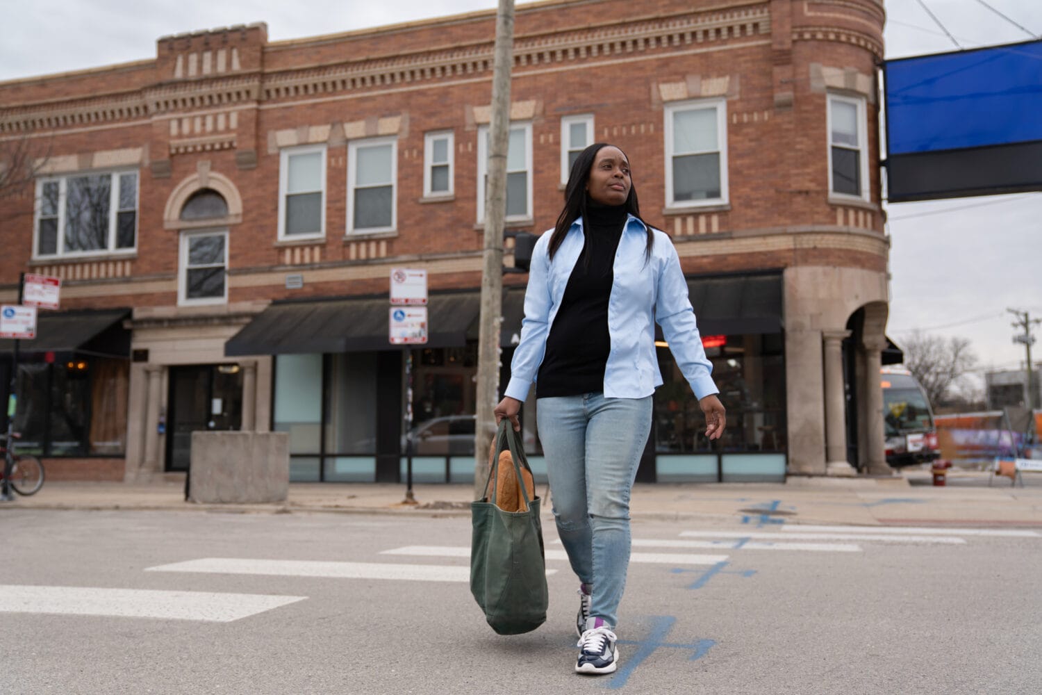 Black woman crosses street with grocery bag before Tuskegee pedestrian accident.