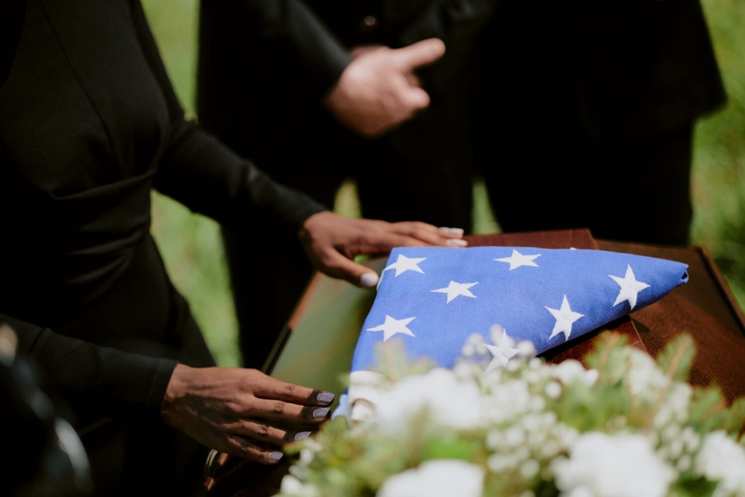 Tuskegee family mourns loved one while standing over a coffin decorated with flowers and a folded flag.