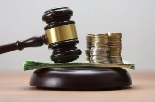 Closeup of gavel, paper currency, and coins stacked on sound block.