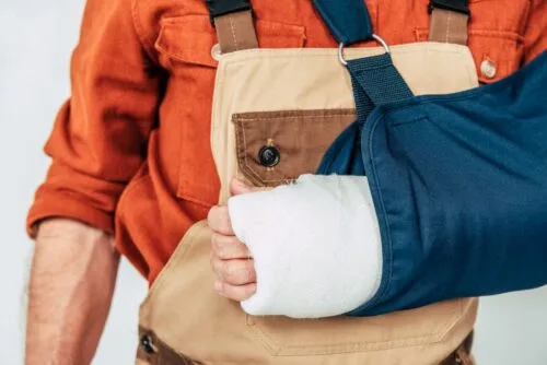 Closeup of injured construction worker wearing overalls and shoulder sling.