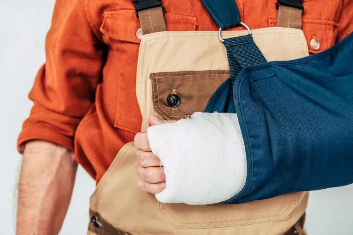 Closeup of injured construction worker wearing overalls and shoulder sling.