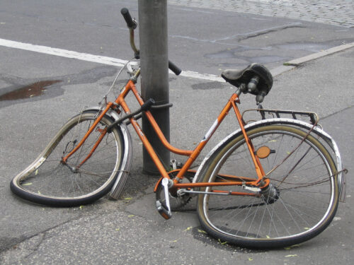 A wrecked orange bicycle locked to a street pole.