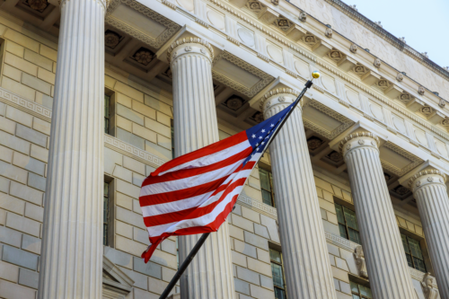 American flag waving in front of a neoclassical federal building.