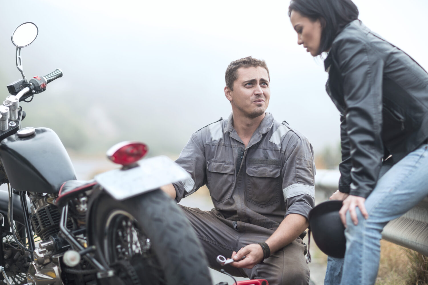 A man and woman wait on the side of the road after a motorcycle accident.