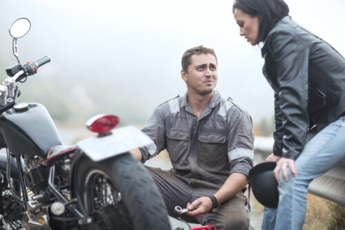 A man and woman wait on the side of the road after a motorcycle accident.