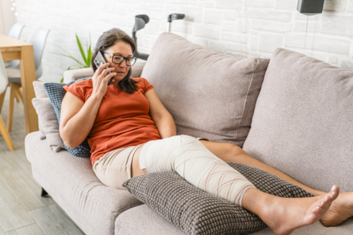 A middle-aged woman with a wrapped, broken leg propped up on a couch.